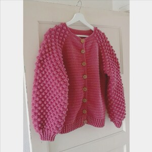 Op de afbeelding: Een roze gebreid vest met knopen en textuur in de mouwen.