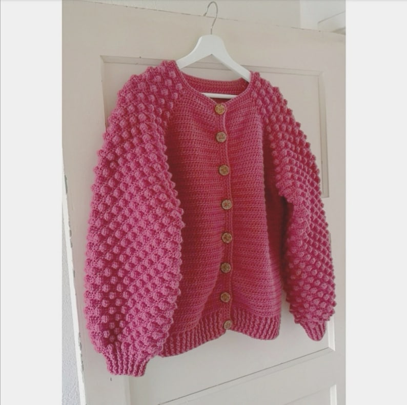 Op de afbeelding: Een roze gebreid vest met knopen en textuur in de mouwen.