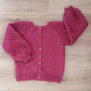 Op de afbeelding: Een roze gebreid vest met knoopsluiting en textuur in de mouwen.