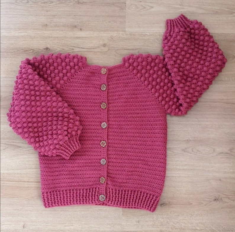 Op de afbeelding: Een roze gebreid vest met knoopsluiting en textuur in de mouwen.