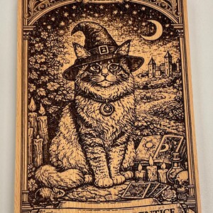 May include: Wooden plaque featuring a detailed illustration of a cat wearing a witch hat, with the text "THE WITCH APPRENTICE". The artwork includes candles, a crescent moon, and a castle, all in a vintage style.
