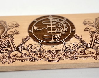 Puede incluir: Una caja de madera con un diseño decorativo que presenta una calavera, esqueletos y un sello. La caja tiene acentos de esquina de metal.
