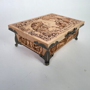 May include: A wooden box with a hinged lid and ornate metal accents. The lid features a woodburned image of two people with the text "It's a good life".