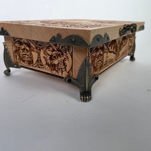 May include: A wooden box with intricate carvings and metal accents. The box has a hinged lid and sits on four decorative feet.