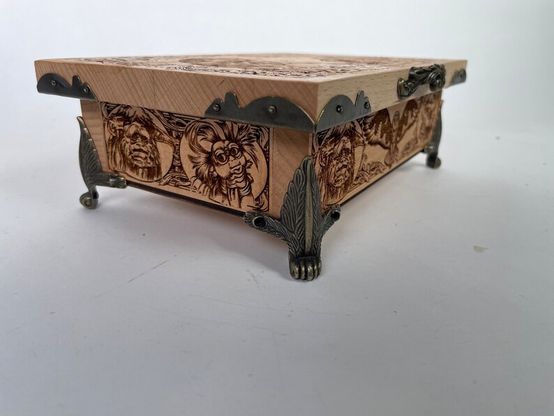 May include: A wooden box with intricate carvings and metal accents. The box has a hinged lid and sits on four decorative feet.