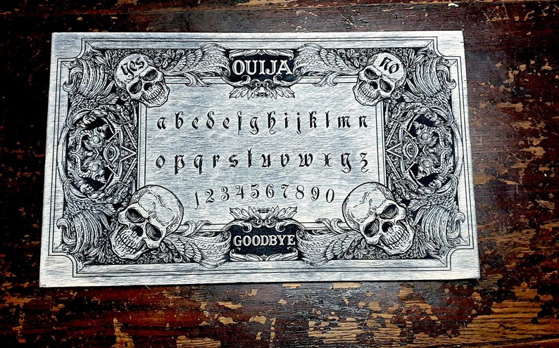 May include: A silver Ouija board with a black and white design. The board features a traditional alphabet, numbers, and the words "yes", "no", and "goodbye".