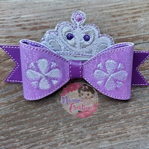 May include: Purple hair bow with a silver embroidered crown and flower designs.