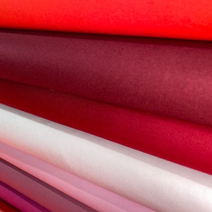 May include: A stack of fabric rolls in various shades of red, pink, and purple. The fabric is smooth and appears to be a soft, velvety material.