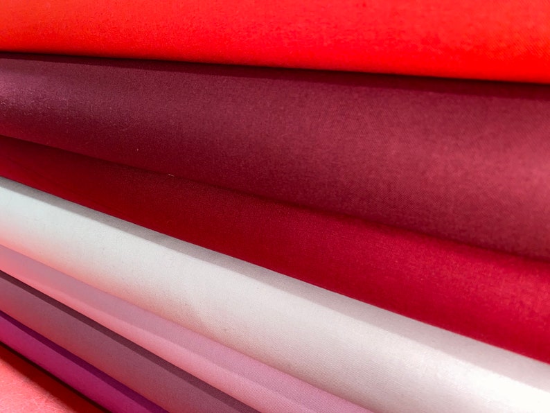 May include: A stack of fabric rolls in various shades of red, pink, and purple. The fabric is smooth and appears to be a soft, velvety material.