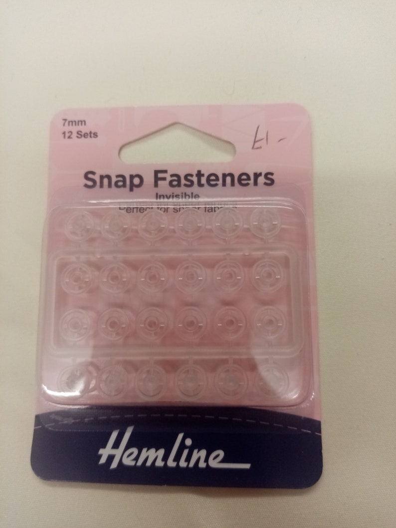 May include: A pack of 12 sets of 7mm clear plastic snap fasteners. The pack is pink and blue and says "Snap Fasteners Invisible" and "Hemline".