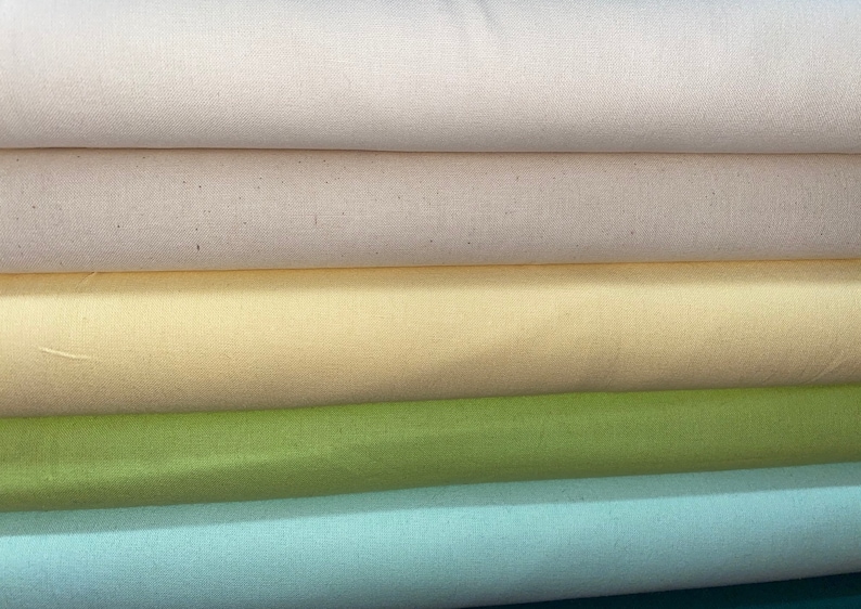 May include: Five rolls of fabric in different colors. The top roll is a light beige, the second roll is a slightly darker beige, the third roll is a pale yellow, the fourth roll is a light green, and the bottom roll is a light blue.