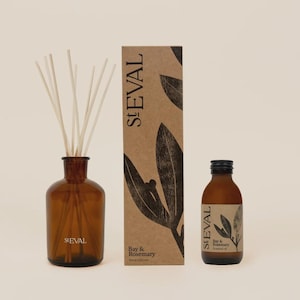 May include: A St. Eval Bay & Rosemary reed diffuser set featuring a brown glass bottle with reeds, a tall rectangular cardboard box with black leaf illustrations, and a smaller brown glass bottle of scented oil with a black screw cap.
