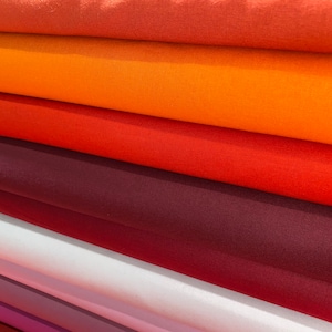 May include: A stack of fabric swatches in various shades of orange, red, and purple. The fabric is smooth and has a subtle sheen.