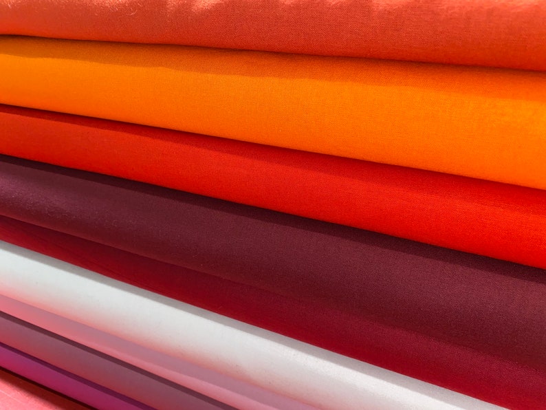 May include: A stack of fabric swatches in various shades of orange, red, and purple. The fabric is smooth and has a subtle sheen.