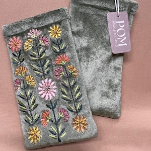 May include: Two sage green velvet pouches with embroidered floral designs in pink, orange, and yellow. One pouch has a tag that reads "POM Peace of Mind". The pouches are rectangular and appear to be made of a soft, plush material.