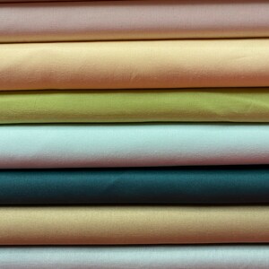May include: A stack of fabric swatches in various colors, including pink, peach, yellow, green, blue, beige, and white. The fabric is smooth and appears to be satin.