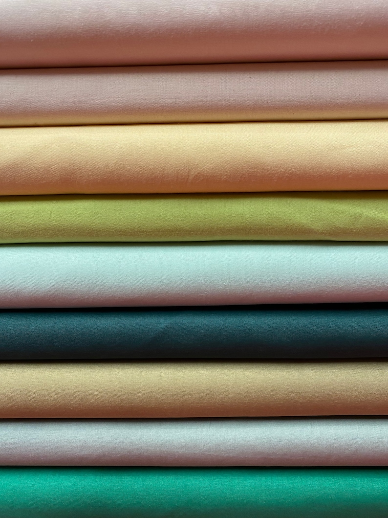 May include: A stack of fabric swatches in various colors, including pink, peach, yellow, green, blue, beige, and white. The fabric is smooth and appears to be satin.