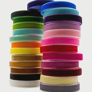 Può includere: Pile di nastri di velluto colorati in varie tonalità, tra cui blu, verde, arancione, giallo, rosa e bordeaux. Il nastro è ordinatamente arrotolato e impilato, mostrando le trame e le variazioni di colore. Ideale per progetti di artigianato e decorazione.