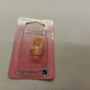 Könnte beinhalten: Verstellbarer Plastik-Fingerhut zum Nähen und Quilten, verpackt in rosa und weißer Verpackung mit dem Hemline-Logo und den Worten "Quality Checked".