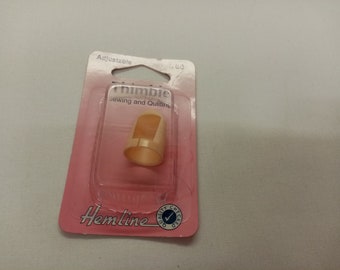 Könnte beinhalten: Verstellbarer Plastik-Fingerhut zum Nähen und Quilten, verpackt in rosa und weißer Verpackung mit dem Hemline-Logo und den Worten "Quality Checked".