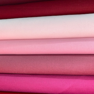May include: Five rolls of fabric in various shades of pink and red. The fabric is a smooth, woven material.
