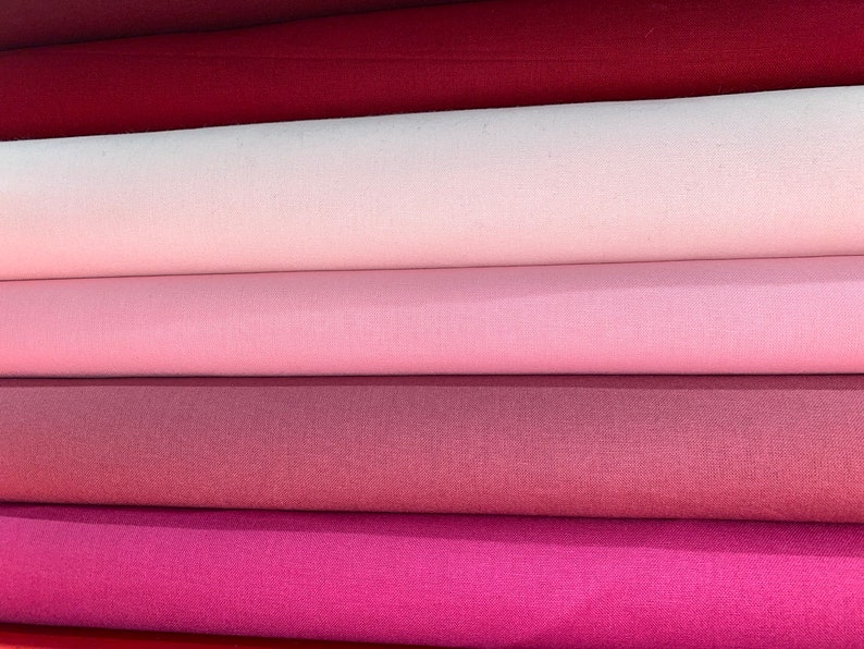 May include: Five rolls of fabric in various shades of pink and red. The fabric is a smooth, woven material.
