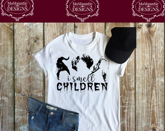 May include: A white short-sleeved t-shirt featuring a black graphic print of three silhouettes and the text "i smell CHILDREN" in a stylized font. The shirt is paired with a black baseball cap and blue denim jeans, displayed as a flat lay.