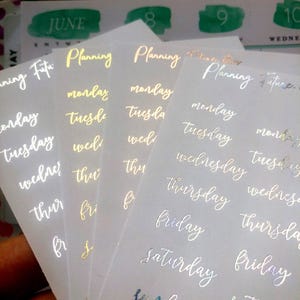 Puede incluir: Hojas de pegatinas para planificador con letras doradas y plateadas. Las pegatinas incluyen los días de la semana y la palabra "Planning". El fondo muestra una página de calendario con el mes de junio.