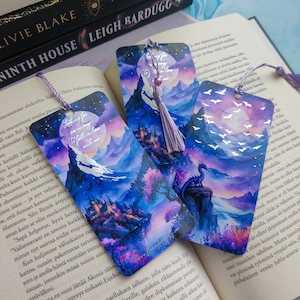 Può includere: Tre segnalibri ad acquerello con un fiocco viola. I segnalibri mostrano una catena montuosa con un castello, un drago e una luna con pipistrelli che volano intorno. Il testo sui segnalibri dice "Looking for an enemy to fall in love with me."