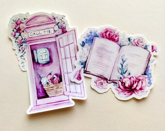 May include: Two die-cut stickers featuring watercolor illustrations. One is a pink telephone booth with the text CALL ME, adorned with pink and blue flowers. The other is an open book surrounded by pink and blue floral arrangements.