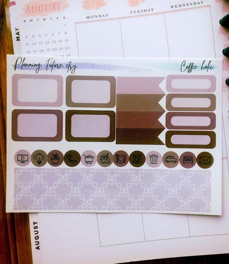 May include: A sticker sheet featuring various planner labels in shades of brown, mauve, and cream. The sheet includes rectangular boxes, flag-shaped markers, rounded icons with black line drawings, and a wide strip with a repeating scalloped pattern.