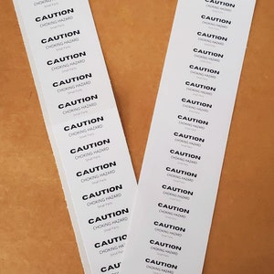 May include: A sheet of white stickers with black text that reads "CAUTION CHOKING HAZARD Small Parts". The stickers are arranged in two columns.
