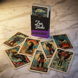 Puede incluir: Un mazo de cartas de tarot "Zen Decks" con una caja negra y morada. Las cartas presentan ilustraciones de figuras con etiquetas de texto. La caja dice "Zen Decks" y "The Original Gift". Las cartas est&aacute;n esparcidas sobre una superficie de m&aacute;rmol.