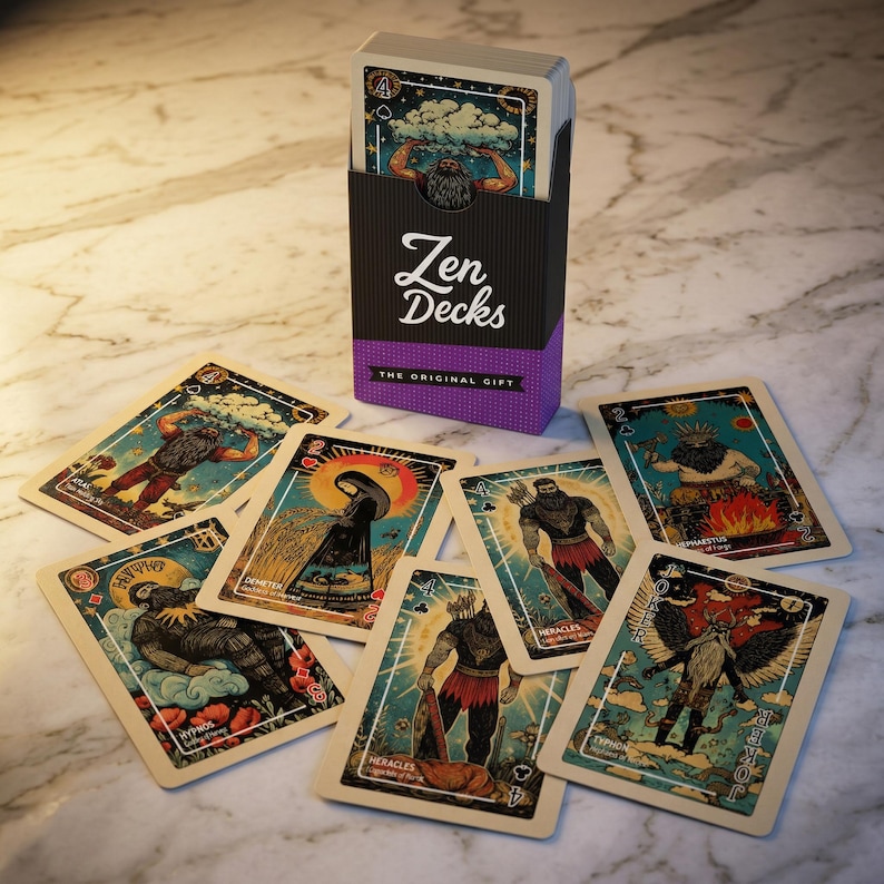 Puede incluir: Un mazo de cartas de tarot "Zen Decks" con una caja negra y morada. Las cartas presentan ilustraciones de figuras con etiquetas de texto. La caja dice "Zen Decks" y "The Original Gift". Las cartas est&aacute;n esparcidas sobre una superficie de m&aacute;rmol.