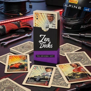 Może przedstawiać: Talia kart do gry "Zen Decks" z czarnym i fioletowym pudełkiem. Karty przedstawiają zdjęcia kierowców wyścigowych i samochodów wyścigowych. Na pudełku widnieje napis "Zen Decks" i "The Original Gift".