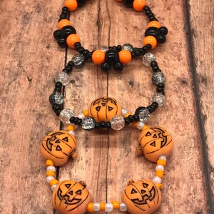 Puede incluir: Tres pulseras con temática de Halloween con cuentas naranjas y negras. La pulsera superior tiene cabezas de Mickey Mouse negras y cuentas naranjas. La pulsera del medio tiene cuentas negras y plateadas. La pulsera inferior tiene cuentas de calabaza naranja y cuentas blancas y naranjas.