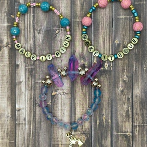 May include: Three beaded bracelets with gold lettering that reads "Make it Pink", "Make it Blue", and a third bracelet with iridescent beads and a gold Mickey Mouse charm.