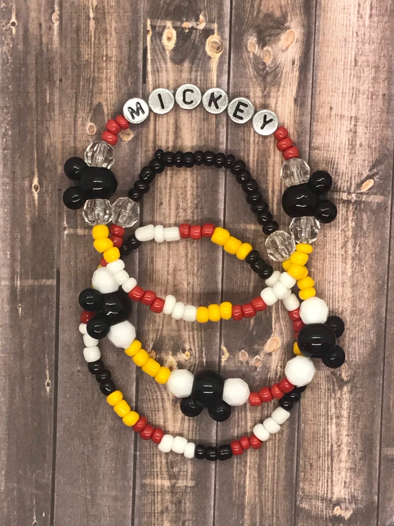 May include: Three beaded bracelets with Mickey Mouse charms. The top bracelet has silver letter beads spelling out "MICKEY". The bracelets are red, white, yellow, and black.