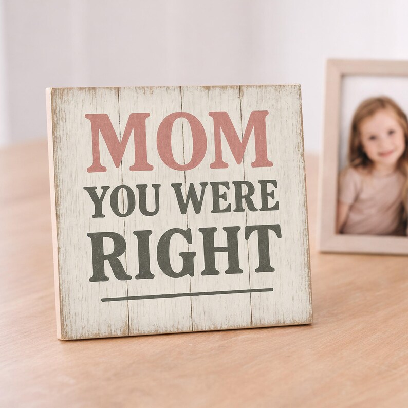 May include: A wooden sign with the words "MOM YOU WERE RIGHT" in pink and gray lettering. The sign has a distressed, rustic look and is placed on a wooden surface. A framed photo is in the background.
