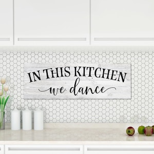 May include: White wooden sign with black text that reads "In this kitchen we dance".
