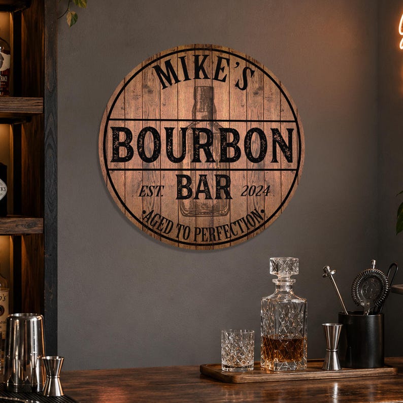 May include: A round wooden sign with the text "Mike's Bourbon Bar" and "Aged to Perfection". The sign has a rustic, barrel-like design. A decanter, glasses, and bar tools are on a wooden tray.