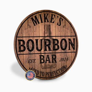 May include: Round wooden sign with the text "MIKE'S BOURBON BAR" and "AGED TO PERFECTION". The sign has a wood grain background and a graphic of a bourbon bottle. Includes a "Made in USA" sticker.