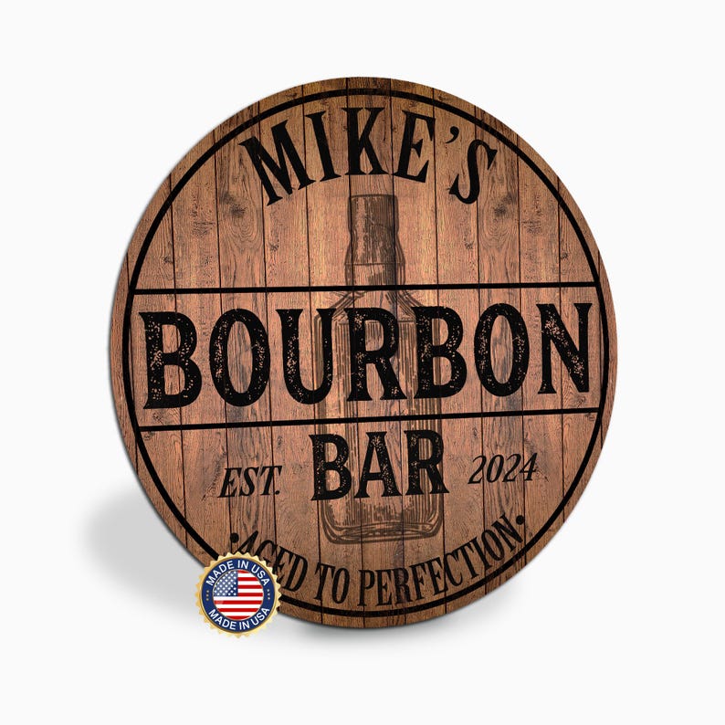 May include: Round wooden sign with the text "MIKE'S BOURBON BAR" and "AGED TO PERFECTION". The sign has a wood grain background and a graphic of a bourbon bottle. Includes a "Made in USA" sticker.