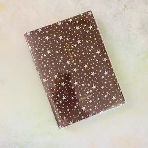 May include: A brown leather-bound journal with a gold foil design of stars and the text "日々を丁寧に" (meaning "Live each day carefully"). The journal is dated 2022-2026.