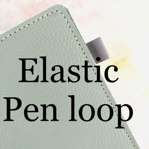 Peut inclure: Gros plan sur un carnet en cuir vert clair avec un bord cousu et une boucle élastique pour stylo. Le texte "Elastic Pen loop" est imprimé sur la couverture.
