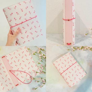 May include: A white planner with a pink floral pattern and a pink elastic closure. The planner is shown in multiple views, including an open layout and a side view, with a pink interior and a pink elastic band.