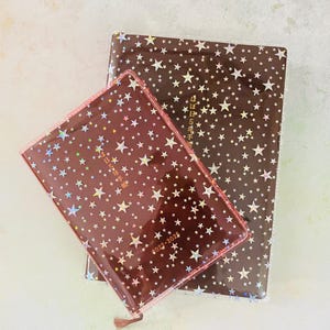 May include: Two brown star-patterned journals with gold foil accents. The smaller journal has the text "2022-2023" printed on the cover. The larger journal has the text "2023年5月始まり" printed on the cover.