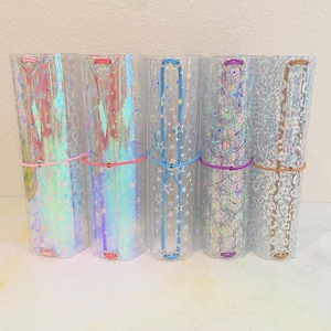 May include: Five clear, cylindrical containers with iridescent designs and colorful elastic bands. The containers feature patterns of stars, swirls, and other shapes. Each container is approximately 8 inches tall.
