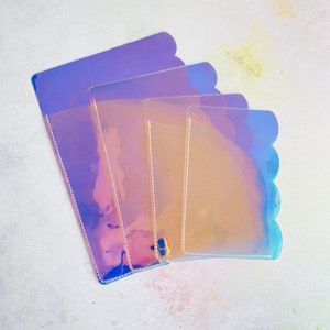 May include: Four iridescent plastic pouches of different sizes, stacked on top of each other. The pouches are translucent and have a scalloped edge.