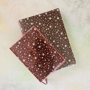 May include: Two brown star-patterned journals with gold lettering. The smaller journal has the text "2022-2025" on the cover.